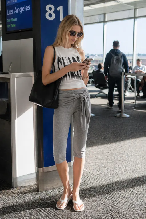 Candid Airport Style outfit featuring a white chaos graphic tank, grey wrap capri leggings, and white sandals